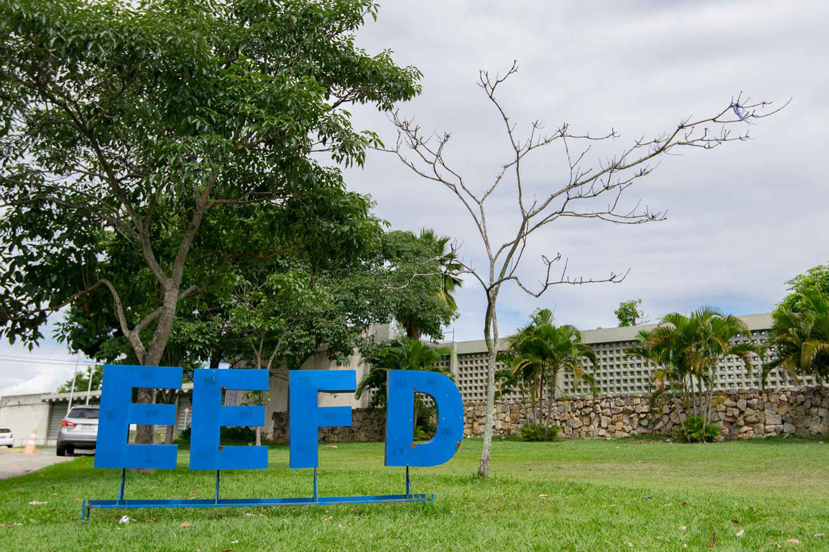 Fotografia, em dia nublado, da Escola de Educação Física e Desportos. Na parte inferior da imagem, está o letreiro EEFD, na cor azul, fixado no gramado.